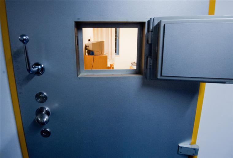 Ein kleines Fenster in einer Zellentür gewährt einen Einblick in eine Gefängniszelle.