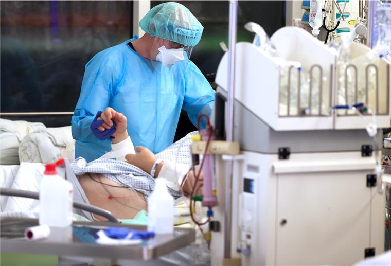 Ein Facharzt versorgt einen Covid-19-Patienten auf der Intensivstation der Leipziger Uniklinik und hält dessen Hand.
