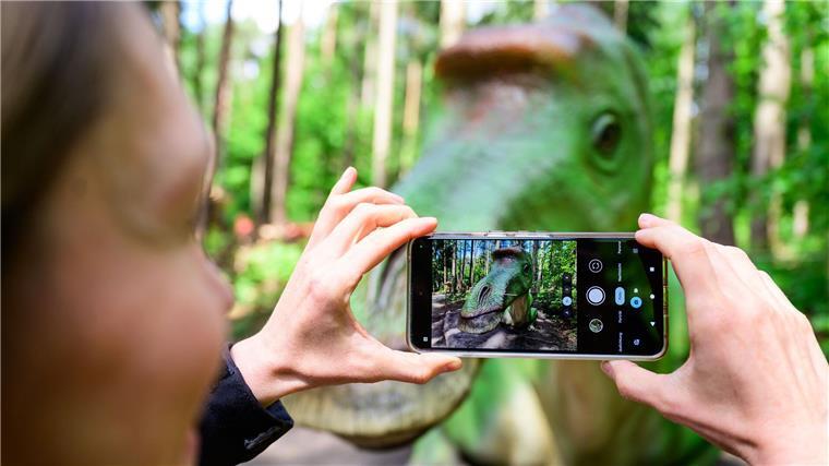 Ein Frau fotografiert im Wildpark Schwarze Berge ein Dinosauriermodell.