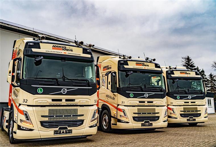 Fuhrunternehmen voll unter Strom: Erste Elektro-Lkw werden in Bremerhaven ausgeliefert Zwei Männer stehen auf einem Lkw Hof vor drei Elektro-Lkws