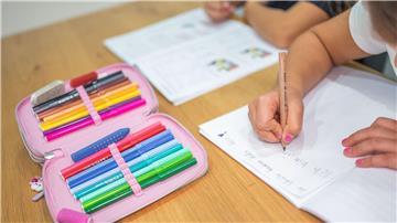 Ein Grundschüler und eine Grundschülerin sitzen in einem Wohnzimmer am Tisch und erledigen Schulaufgaben.