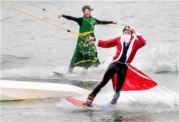 Die Teilnehmer Wilke (vorne) und Johann fahren, verkleidet als Weihnachtsmann und Tannenbaum, mit ihren Wakeboards über einen Badesee 