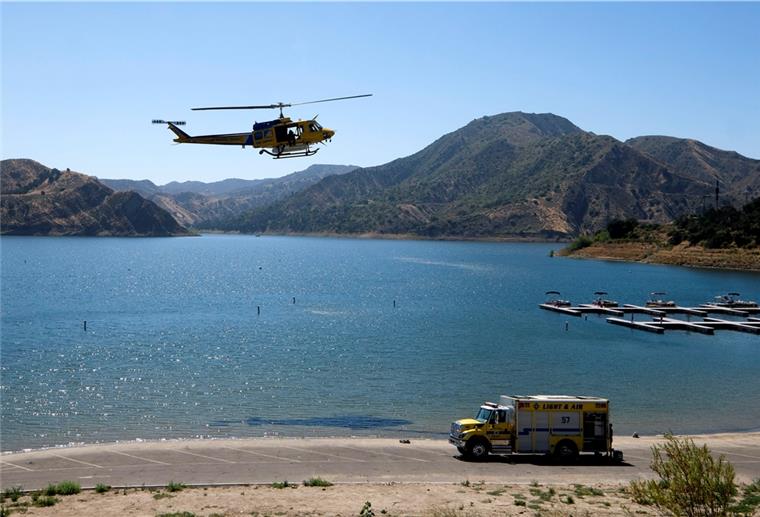 Ein Hubschrauber fliget über den Lake Piru, während weitere Einsatzkräfte an Land nach der US-Schauspielerin Naya Rivera suchen.