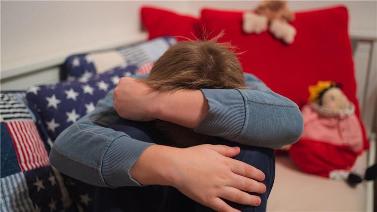 Mehr Hilfen für Schüler bei psychischen Problemen gefordert Ein Junge kauert sich auf seinem Bett zusammen.