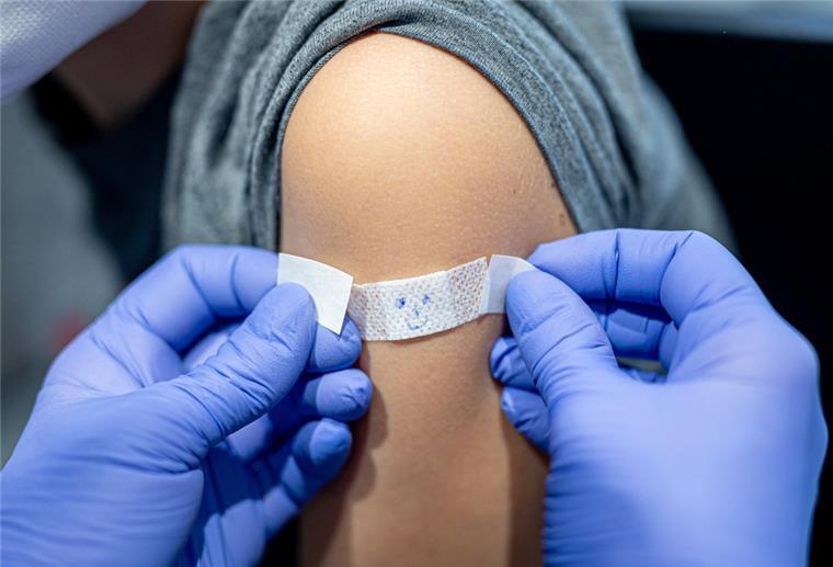 Neue Impfregeln gelten ab Oktober Ein JUnge lässt sich nach seiner Impfung gegen das Coronavirus ein Pflaster mit aufgemaltem Gesicht auf den Arm kleben.