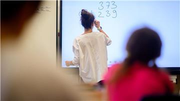 Ein Lehrerin schreibt eine Mathematikaufgabe auf eine digitale Schultafel im Klassenraum einer 4.