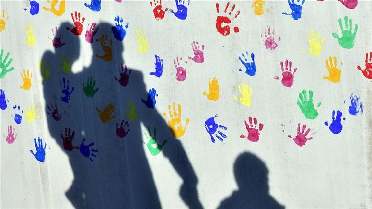 Jedes fünfte Kind in Niedersachsen von Armut bedroht Ein Mann mit einem Kind auf dem Arm und einem an der Hand wirft einen Schatten auf eine mit bunten Handabdrücken bemalte Wand.