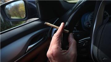 Ein Mann sitzt mit einem Joint zwischen den Fingern am Steuer eines Autos.
