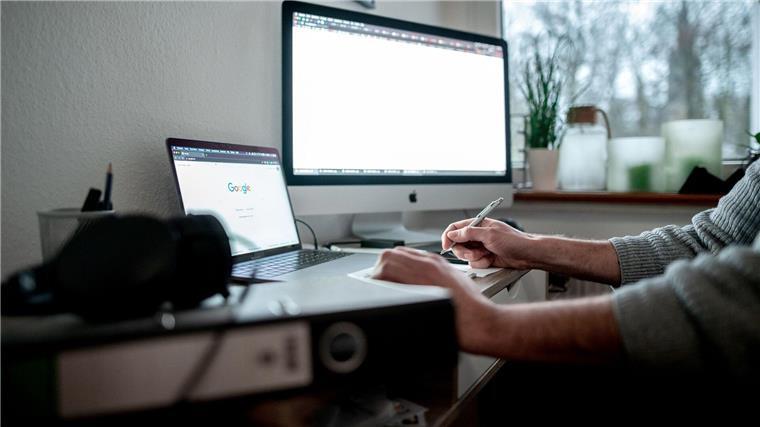 Grüne fordern Tarifvertrag für studentische Hilfskräfte Ein Mann sitzt mit einem Laptop und einem Bildschirm an einem Tisch im Homeoffice.