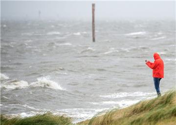 Ein Mann steht bei peitschenden Wellen an einem Strandabschnitt der Nordsee.