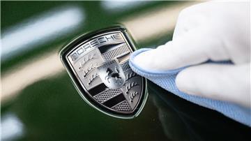 Ein Mitarbeiter der Porsche AG reinigt im Stammwerk in Zuffenhausen das Porsche-Wappen auf der Motorhaube eines vollelektrischen Porsche Taycan, nachdem er es angebracht hat.
