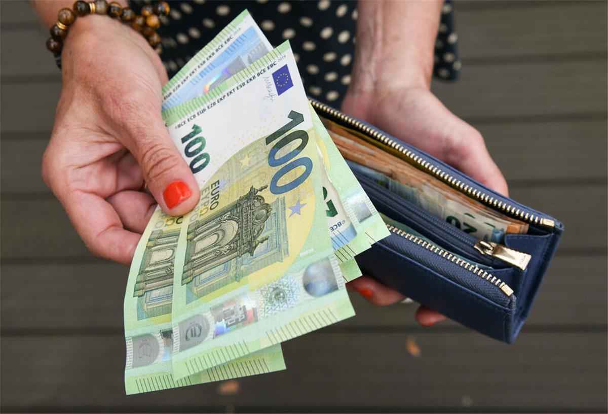 Eine Frau hält eine mit mehreren Geldscheinen gefüllte Geldbörse in einer Hand