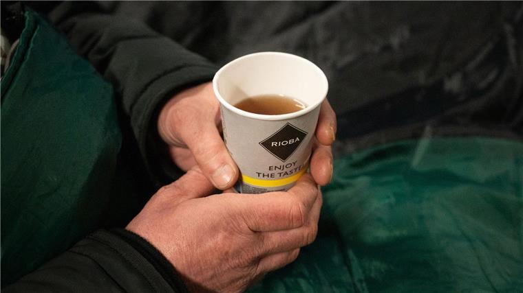 Ein Obdachloser hält einen Becher Tee in der Hand.