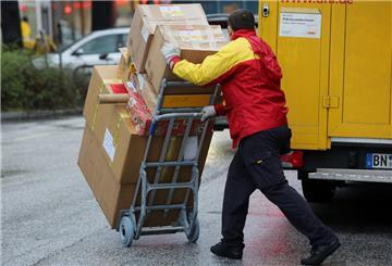 Ein Paketbote der Post schiebt eine Sackkarre mit Paketen über Straße.