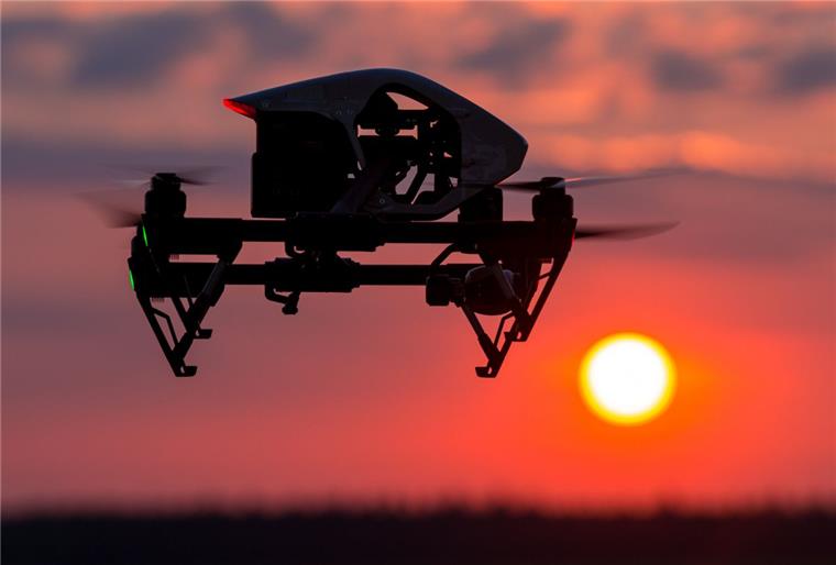 Gefährliche Begegnung: Drohne behindert Lufthansa-Airbus bei Landeanflug Ein Quadrocopter (Drohne) fliegt im Sonnenuntergang über einem Feld.