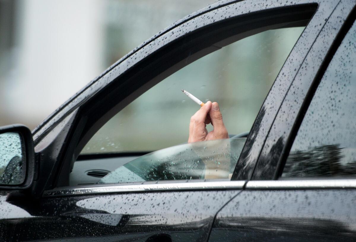Eine Person raucht eine Zigarette beim Autofahren. 