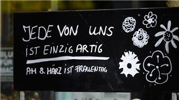 Ein Schriftzug „Jede von ist einzigartig - Am 8. März ist Frauentag“ steht auf einem Schild vor einem Blumenladen.