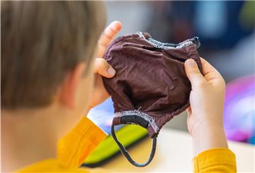 Ein Schüler einer ersten Grundschulklasse hält im Klassenzimmer einen Mundschutz in den Händen.