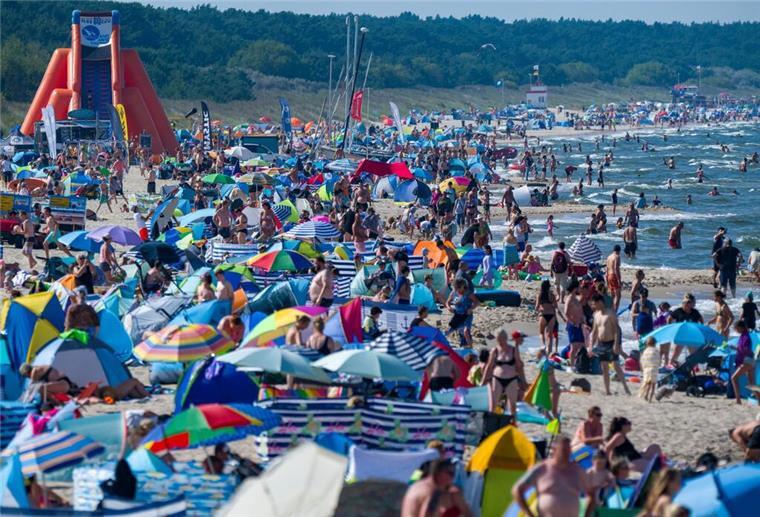 Touristen halten sich bei Sonne und hochsommerlichen Temperaturen im Ostseebad am Strand und im Wasser auf.