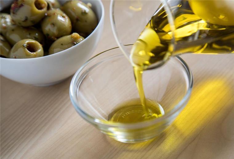Olivenöl im Test: Das sind die besten Produkte - und ihr kriegt sie beim Discounter Olivenöl wird in eine Glasschale gefüllt während im Hintergrund eine Schale mit grünen Oliven steht. Ein Test legt offen, welches Olivenöl besondere Qualität hat.
