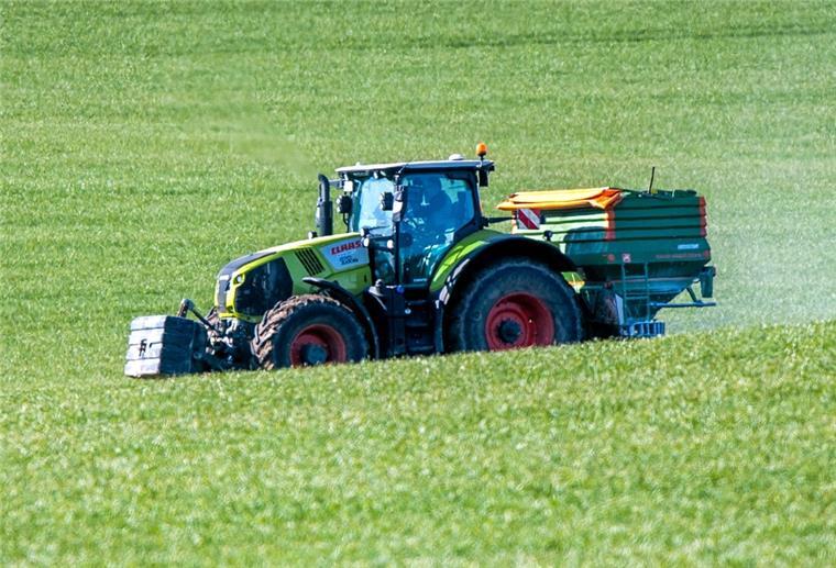 Ein Traktor mit einem Streuaufsatz verteilt Dünger auf einem Feld. Viele Landwirte haben mit massiv gestiegenen Kosten für Düngemittel zu kämpfen.