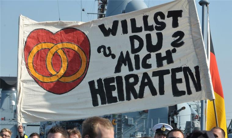Außergewöhnliche Heiratsanträge - in Bremerhaven und weltweit Ein Transparent mit einem Heiratsantrag wird am Freitag auf dem Deck einer Fregatte im Marinestützpunkt Wilhelmshaven hochgehalten.