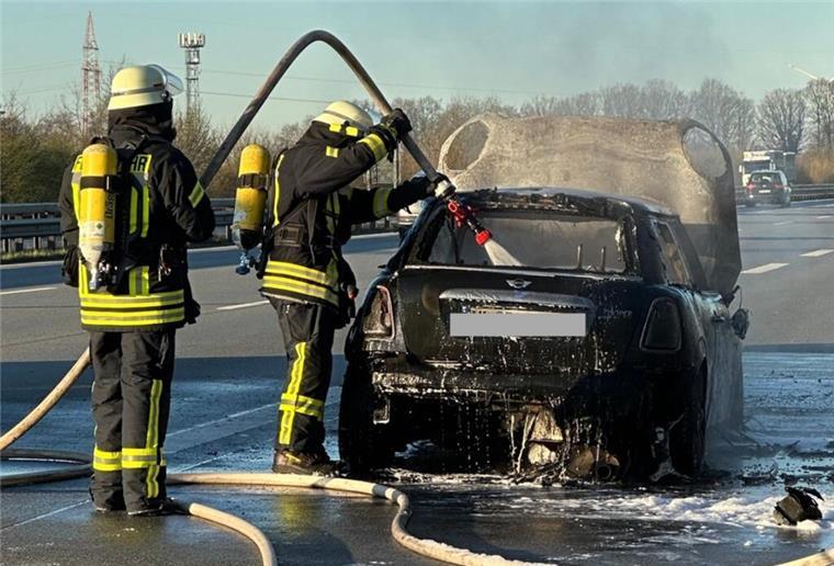 Mini Cooper auf der A1 in Flammen – Feuerwehr im Einsatz Feuerwehrleute löschen ein Auto auf der Autobahn