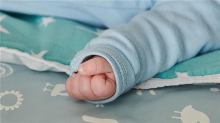 Ein wenige Wochen altes Baby ballt seine Hand zu einer kleinen Faust.