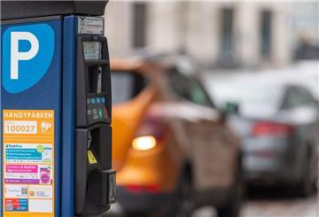 Ein Parkscheinautomat steht vor parkenden Autos.