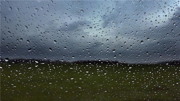 Eine Autoscheibe ist vor dunklen Wolken mit Regentropfen bedeckt.