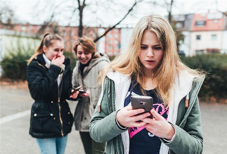 Bremer Soziologin warnt: Mobbing ist zur Volkskrankheit geworden Ein Mädchen steht im Hof einer Schule und schaut auf ihr Smartphone, während im Hintergrund zwei andere Mädchen lachen