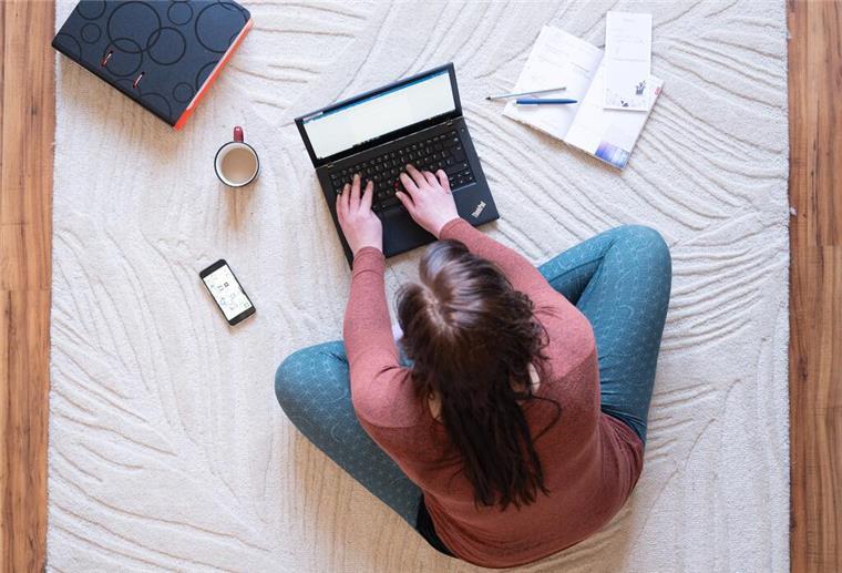 Halbtags freinehmen: Wann das rechtlich möglich ist Eine Frau sitzt im Homeoffice auf einem Teppich und arbeitet an einem Laptop.