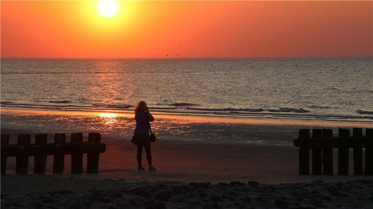 Von Feuershow bis Wattwanderung: Inseln feiern Mittsommer Eine Frau fotografiert am Strand der Insel Wangerooge einen Sonnenuntergang.
