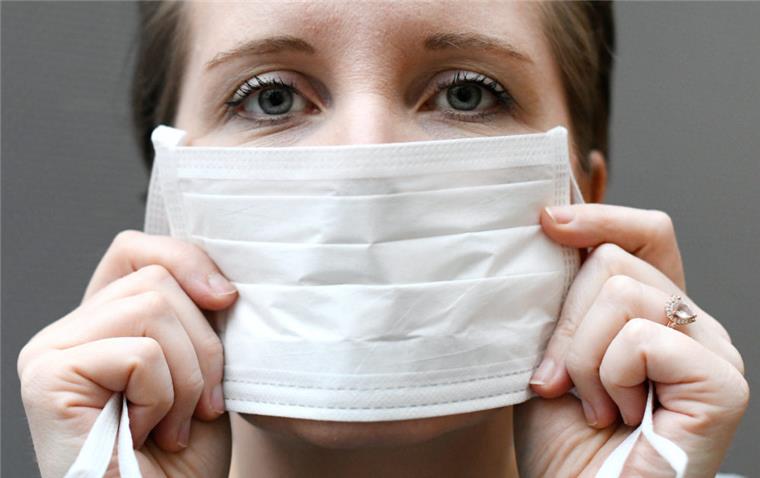 Drei neue Fälle des Coronavirus in Deutschland Eine Frau hält einen Mundschutz vor ihrem Gesicht.