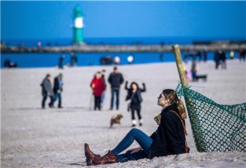 Eine Frau sitzt am Strand von Warnemünde und sonnt sich.