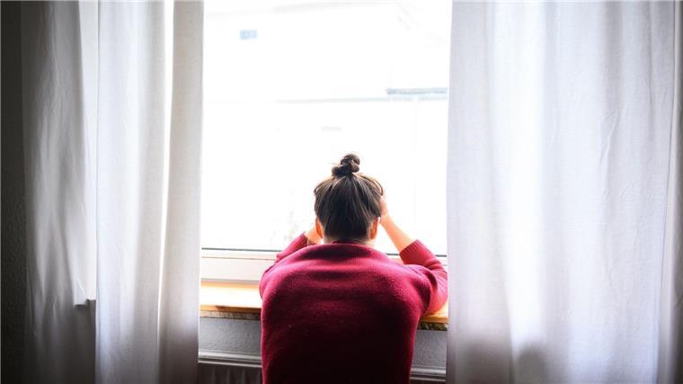 Eine Frau sitzt mit Kopf in den Händen am Fenster.