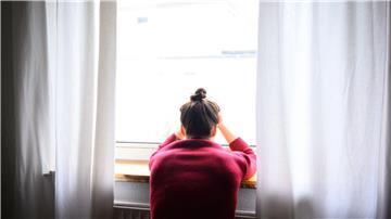 Eine Frau sitzt mit Kopf in den Händen am Fenster.