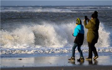 Eine Frau steht mit einem Kind am Strand vor den tosenden Wellen der Nordsee. 