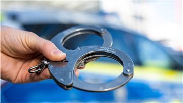 Eine Hand hält Handschellen vor einen Streifenwagen der Polizei.
