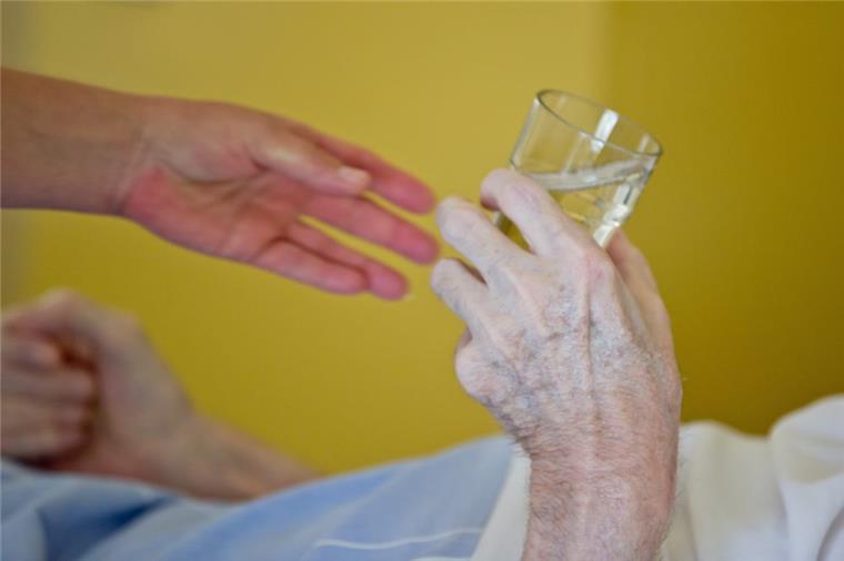 Noten für Pflege-Heime sollen realistisch werden Eine Krankenpflegerin reicht einem Patienten in ein Glas Wasser.