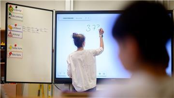 Eine Lehrerin schreibt eine Mathematikaufgabe auf eine digitale Schultafel.