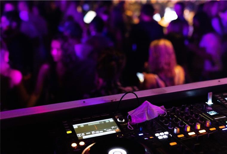 Eine Maske liegt auf dem Mischpult, vor dem Menschen tanzen im Club. Über die Weihanchtstage werden diese in Niedersachsen geschlossen bleiben.