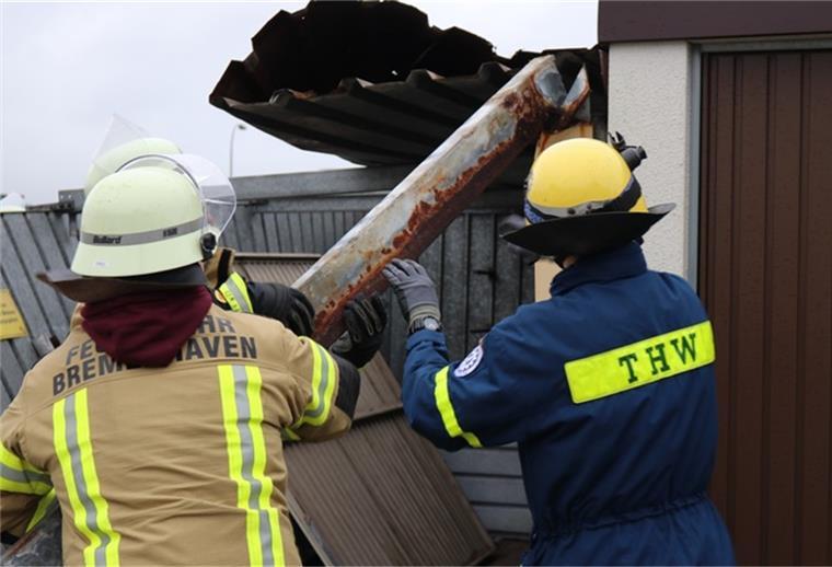 Sturm in Bremerhaven: 38 Einsätze für die Feuerwehr Zwei Feuerwehrmänner stehen vor einer demolierten Garage und manövrieren ein Stück Metall.