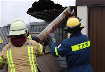 Zwei Feuerwehrmänner stehen vor einer demolierten Garage und manövrieren ein Stück Metall.