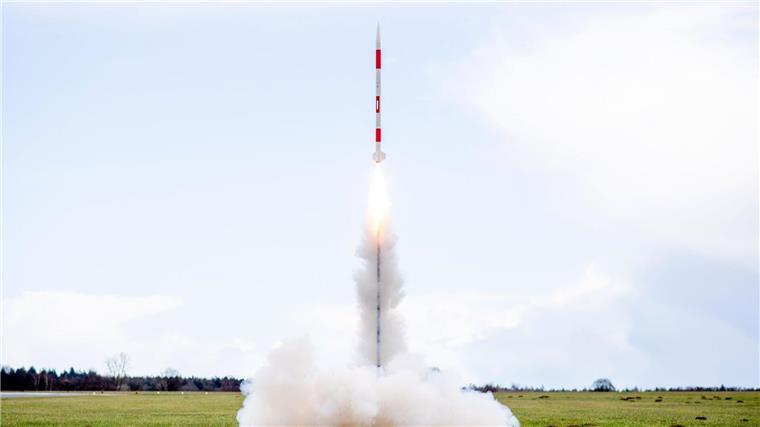 Schülerteam gewinnt deutschen Minisatelliten-Wettbewerb Eine mit mehreren Minisatelliten bestückte Rakete startet 2023 von einer Wiese auf dem Flugplatz.