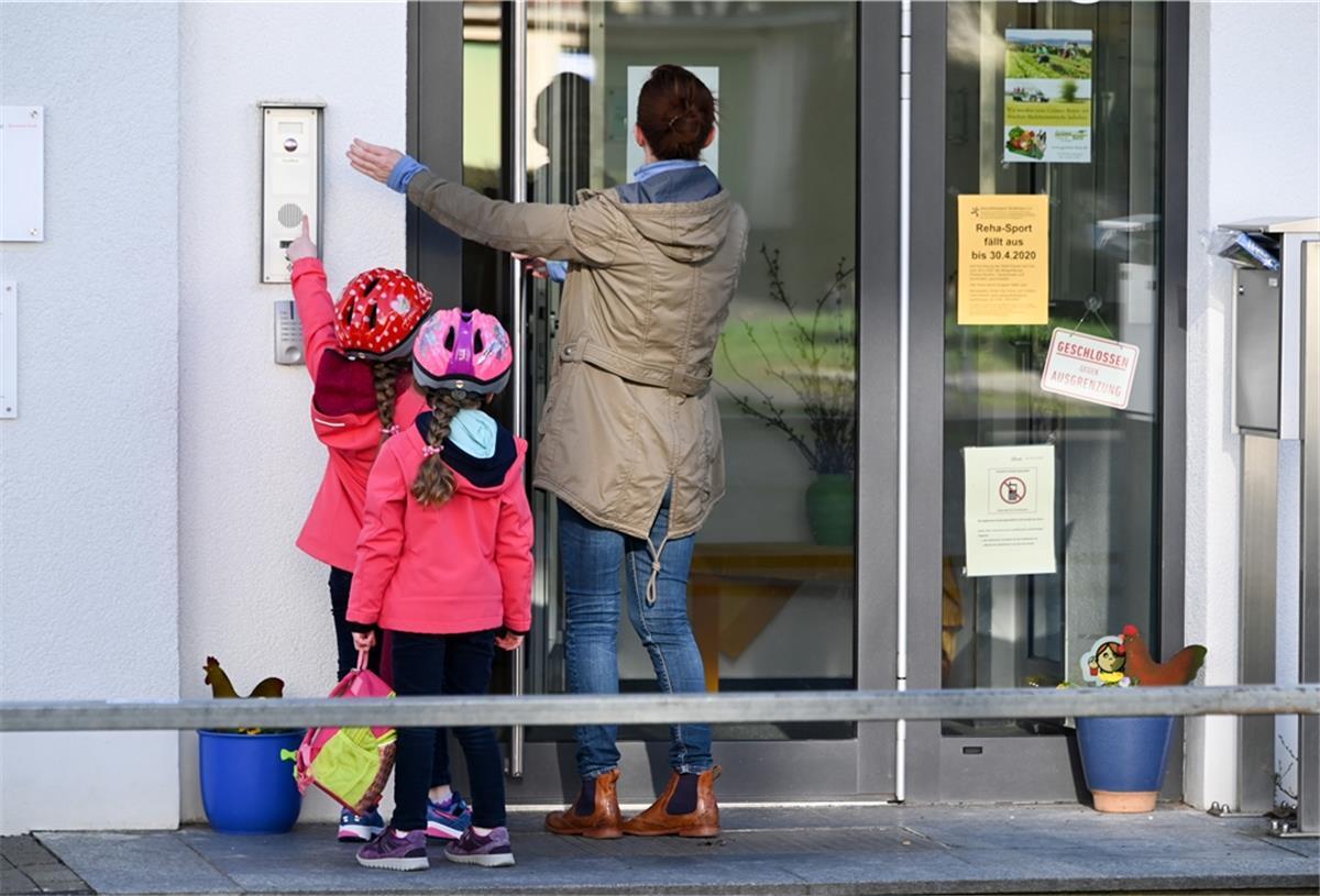 Eine Mutter steht mit ihren Kindern vor dem Kita-Eingang und klingelt.