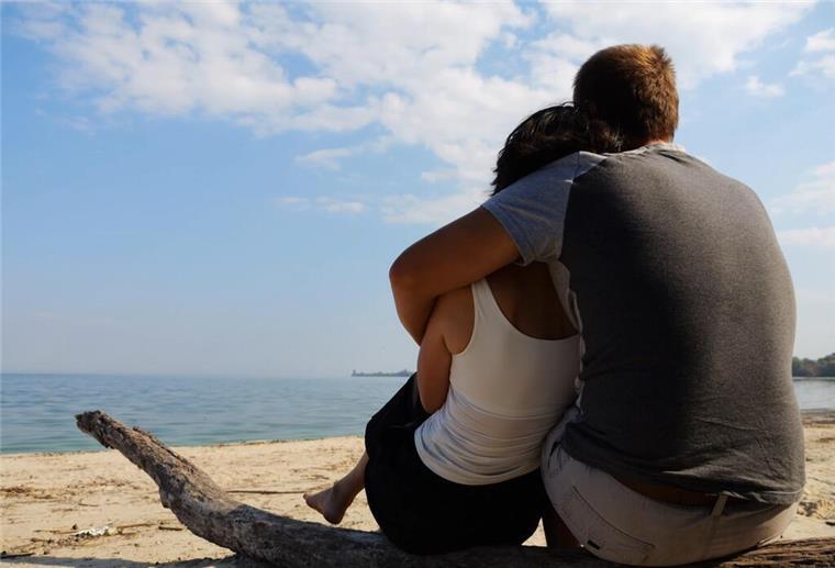 Ein Paar sitzt eng umschlungen an einem Strand und schaut aufs Meer.  Eine neue Methode wirbelt die Partnersuche durcheinander: Frauen visualisieren ihren Wunschpartner auf einem lebensgroßen Foto – und ziehen so Mr. Perfect in ihr Leben.