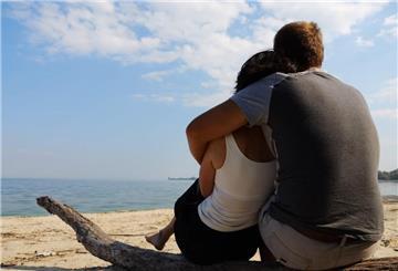 Ein Paar sitzt eng umschlungen an einem Strand und schaut aufs Meer.  Eine neue Methode wirbelt die Partnersuche durcheinander: Frauen visualisieren ihren Wunschpartner auf einem lebensgroßen Foto – und ziehen so Mr. Perfect in ihr Leben.