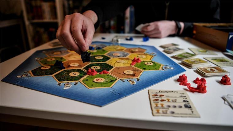 Eine Person spielt das Brettspiel Siedler von Catan. 