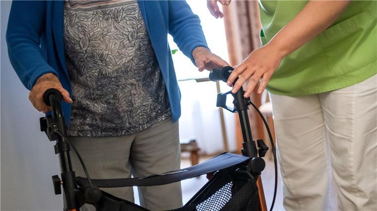 Kabinett beschließt neue Förderung für Pflegeeinrichtungen Eine Pflegefachkraft hilft einer Bewohnerin in einem Seniorenheim mit ihrem Rollator.